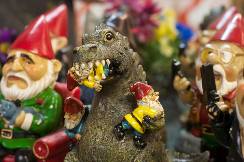A toy Godzilla with a gnome in its mouth, another in its arm, surrounded by an army of more gnomes, each gnome a metaphor for images lacking alt tags!