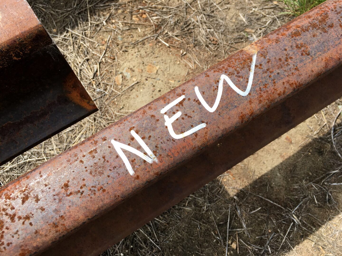 The word "New" hand written atop a rusted iron rail of a train track.